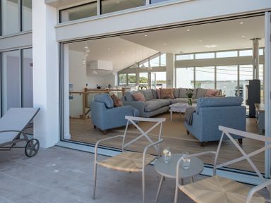 A seating area with two chairs and a side table on a patio overlooking a living room with sofas and a coffee table at Point Break in Polzeath