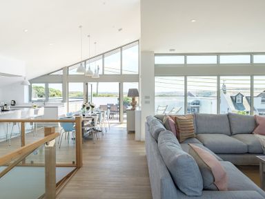 An open plan living and dining area with grey sofas and a dining table set at Point Break in Polzeath