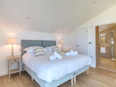 A bedroom with a bed two bedside tables with lamps and an en suite bathroom at Point Break in Polzeath