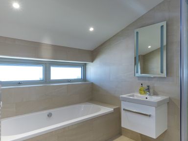 A bathroom with a bathtub a sink with a mirror and two windows at Point Break in Polzeath