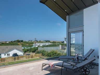 A patio with two lounge chairs and a glass door overlooking houses and fields at Point Break in Polzeath