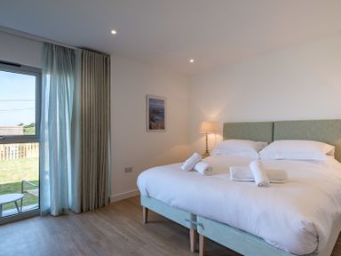 A bedroom with a double bed white linens towels a lamp and a glass door with curtains at Point Break in Polzeath