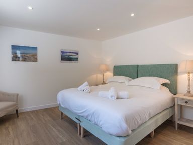 A bedroom with a double bed white bedding rolled towels bedside tables lamps a chair and two framed pictures on the wall at Point Break in Polzeath