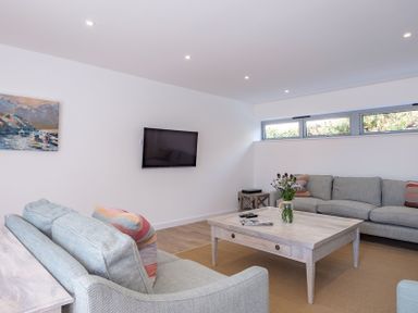 A living room with two sofas a wooden coffee table with flowers a wall mounted television and a painting on the wall at Point Break in Polzeath