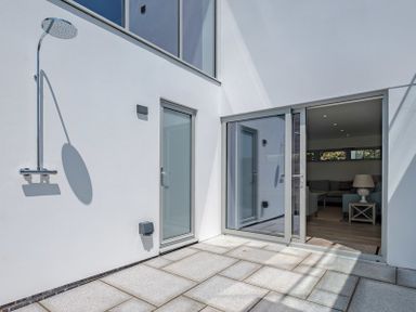 A patio area with a wall-mounted outdoor shower and a glass sliding door leading to a living room at Point Break in Polzeath