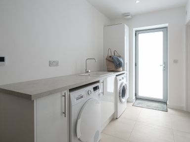 A laundry room with a washing machine, dryer, sink, cabinet, and a door at Point Break in Polzeath