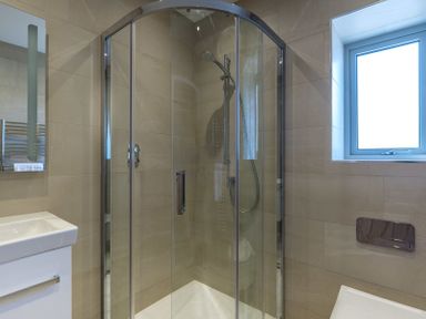 A bathroom with a glass shower enclosure a sink and a window at Point Break in Polzeath