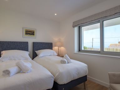 A bedroom with two single beds and rolled towels on them by a window with a view at Point Break in Polzeath