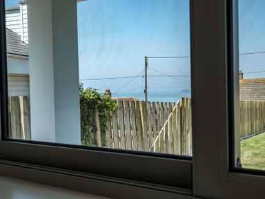 A view of a fence and rooftops with the sea and sky in the background seen through a window at Point Break in Polzeath