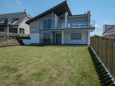 A backyard with lawn and a modern two story house with glass windows and a balcony at Point Break in Polzeath