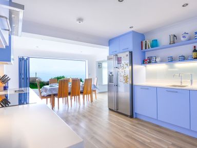 A kitchen with blue cabinets a stainless steel refrigerator and a dining area with wooden chairs at Sea Mist in Polzeath