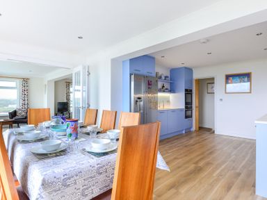 A dining table set with tableware in a kitchen with blue cabinets and wooden floor at Sea Mist Polzeath
