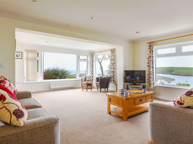 A living room with sofas a coffee table a television and windows overlooking the sea at Sea Mist in Polzeath