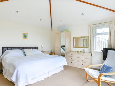 A bedroom with a bed a wooden wardrobe a dresser with a mirror and a chair by the window at Sea Mist in Polzeath