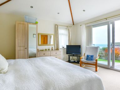 A bedroom with a bed dresser wardrobe a chair and a television with a sea view at Sea Mist in Polzeath