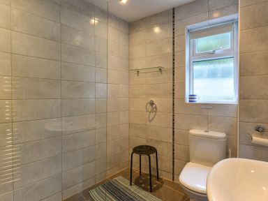 A bathroom with a toilet a sink a stool a towel ring and a window at Sea Mist in Polzeath