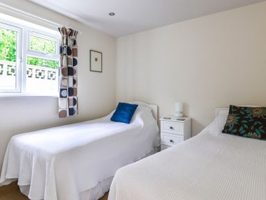 A bedroom with two single beds a nightstand and a window with patterned curtains at Sea Mist in Polzeath