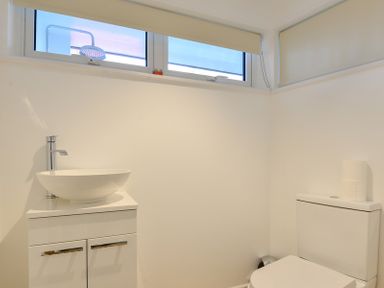 A bathroom with a round sink on a cabinet and a toilet with a roll of toilet paper on the tank at Sea Mist in Polzeath