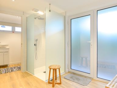 A bathroom with a walk-in shower with frosted glass panels a wooden stool a sink cabinet and frosted glass doors at Sea Mist in Polzeath