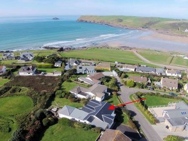 An aerial view of houses near a coastline with a beach and green fields at Sea Mist in Polzeath