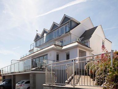 A modern multi-story house with glass balconies and metal railings and cars parked underneath