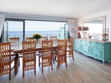 A dining room with a wooden table and chairs with a seaside view at The Crows Nest in Port Isaac