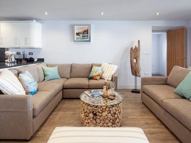A living room with beige sofas cushions a round glass coffee table and a wooden sculpture at The Crows Nest in Port Isaac