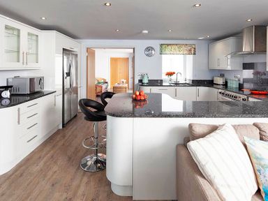 A kitchen with white cabinets black countertops breakfast bar with stools and a sofa at The Crows Nest in Port Isaac