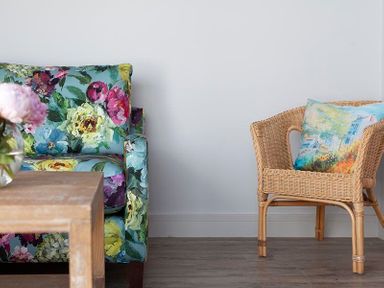 A floral patterned armchair next to a wicker chair with a cushion and a wooden table in front