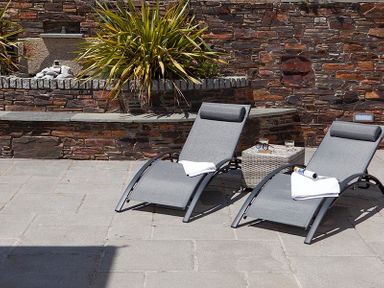 An outdoor patio with two grey loungers and a small table between them against a stone wall at The Crows Nest in Port Isaac