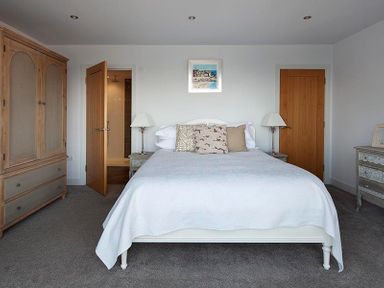 A bedroom with a bed pillows bedside tables lamps and wooden wardrobes at The Crows Nest in Port Isaac