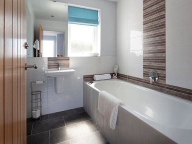 A bathroom with a bathtub a towel on the bathtub and a sink under a window at The Crows Nest in Port Isaac