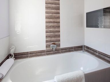 A bathroom with a white bathtub and striped brown and white tiles on the walls at The Crows Nest in Port Isaac