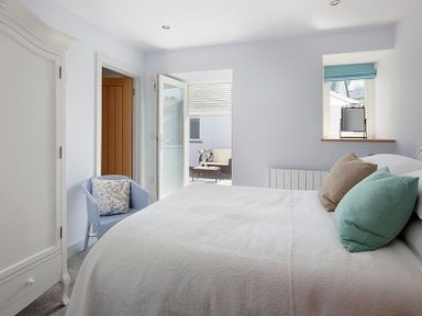 A bedroom with a bed pillows an armchair open door and window at The Crows Nest in Port Isaac