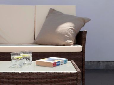 A wicker sofa with white cushions a gray pillow two glasses with lime slices and a book on a glass table at The Crows Nest in Port Isaac