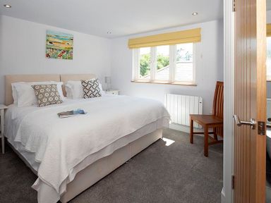 A bedroom with a double bed bedside tables a wooden chair and a window with a yellow blind at The Crows Nest in Port Isaac