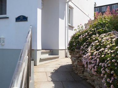 An outdoor pathway with stone steps railing and flower bushes at The Crows Nest in Port Isaac