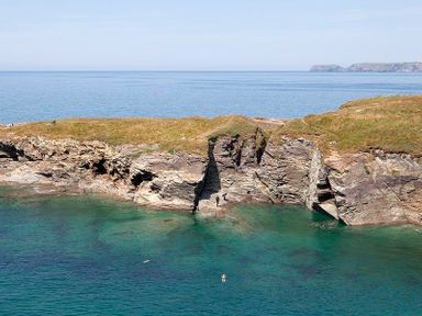 Rocky coastline with clear blue water and people swimming at The Crows Nest in Port Isaac