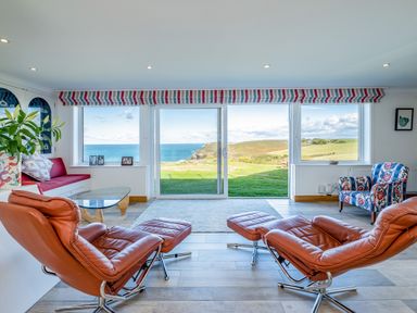 A living room with leather recliner chairs glass coffee table and large windows showing a sea view at Trevan House Lundy in Polzeath