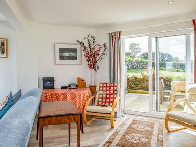 A sitting area with two armchairs a wooden table a sofa and patio doors leading outside at Trevan House Lundy in Polzeath