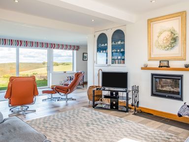 A living room with orange leather chairs and a fireplace at Trevan House (Lundy) in Polzeath