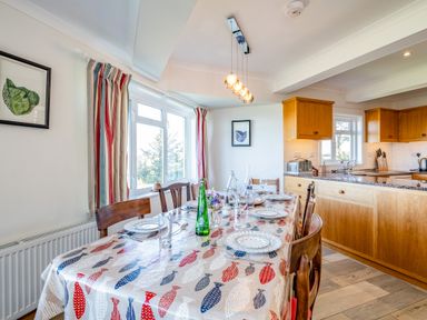 A dining area with a table set for six next to a kitchen with wooden cabinets at Trevan House Lundy in Polzeath
