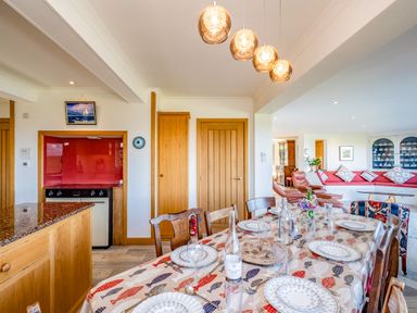A dining area with a table set for a meal and a living room with armchairs and a built-in seating area at Trevan House (Lundy) in Polzeath
