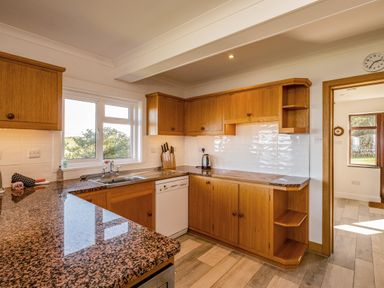 A kitchen with wooden cabinets granite countertops a sink dishwasher and a kettle at Trevan House Lundy in Polzeath