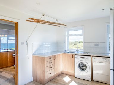 A laundry room with a washing machine a dryer a sink wooden cabinets and a drying rack at Trevan House Lundy in Polzeath