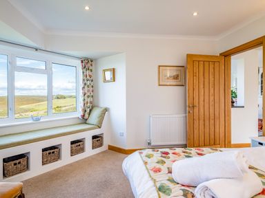 A bedroom with a window seat and storage baskets and open wooden door at Trevan House Lundy in Polzeath