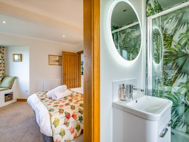 A bedroom with a bed and rolled towels and a bathroom with a sink and round mirror with wall tiles at Trevan House Lundy in Polzeath