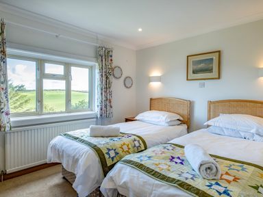 A bedroom with two single beds next to a window showing a green landscape at Trevan House Lundy in Polzeath