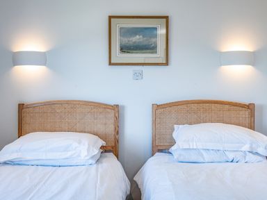 A bedroom with two single beds with wicker headboards and white bedding at Trevan House Lundy in Polzeath