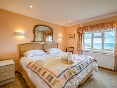 A bedroom with a double bed two rolled towels on the bed a window overlooking the sea and peach colored walls at Trevan House Lundy in Polzeath